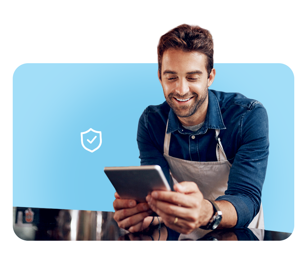 Smiling man using tablet and laptop, highlighting FrankCrum’s competitive workers' compensation coverage and expert claims support