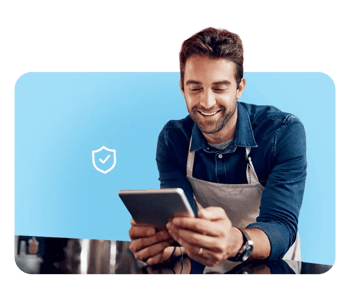 Smiling man using tablet and laptop, highlighting FrankCrum’s competitive workers' compensation coverage and expert claims support