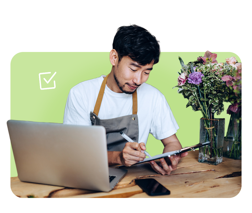 Business owner managing paperwork on laptop, representing FrankCrum’s proactive compliance support and risk reduction services