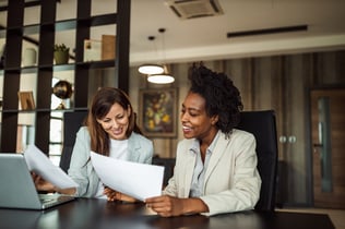 Tenured employee reviews paperwork with coworker.