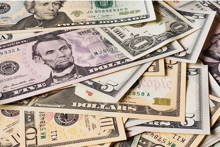 Various types of monetary bills are scattered on a flat surface on top of eachother