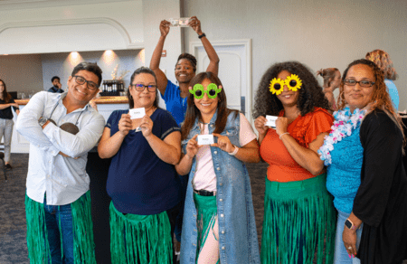 Team members holding game cards, some wearing flower-shaped sunglasses, exuding a fun and friendly atmosphere.