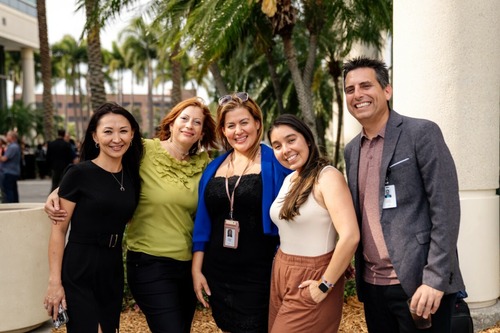 Five team members smiling outside in the courtyard, celebrating the company's anniversary.